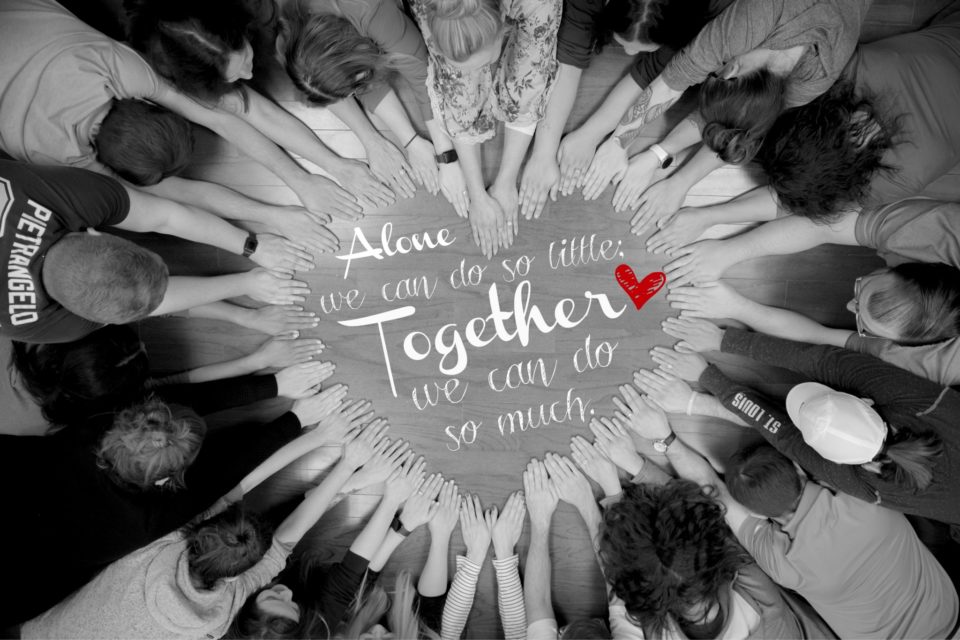 Group of people forming a heart with their hands, with the words - Alone, we can do so little. Together, we can do so much.