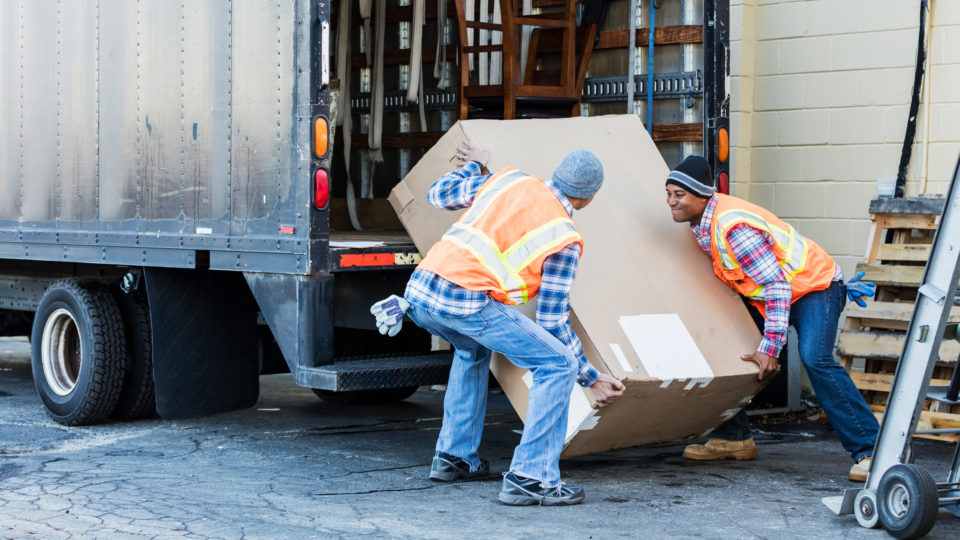 Two men load an oversized box into the back of a cargo truck