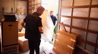 Two movers unload furniture from a large truck