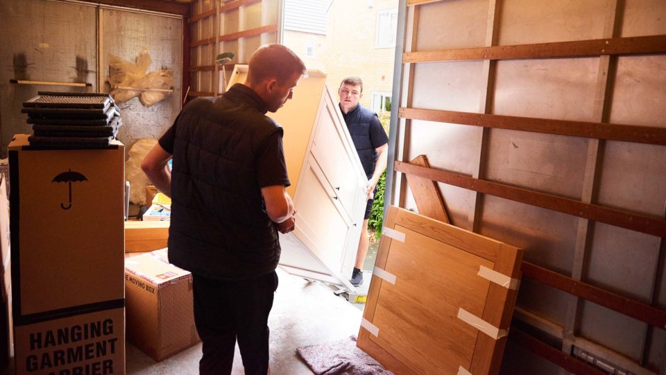 Two movers unload furniture from a large truck