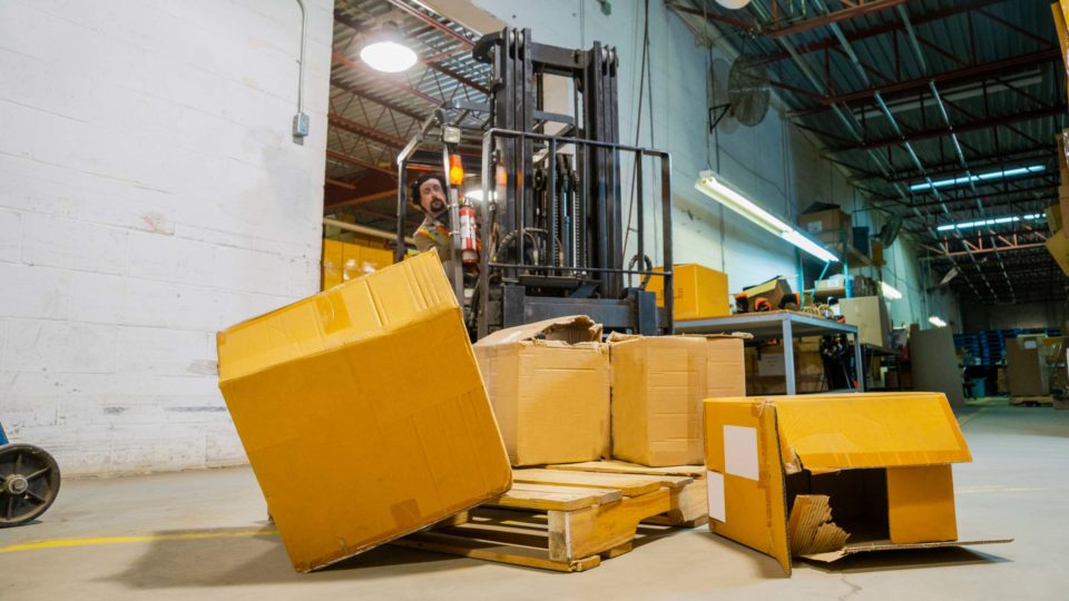 A warehouse employee driving a forklift spills boxes off the forklift